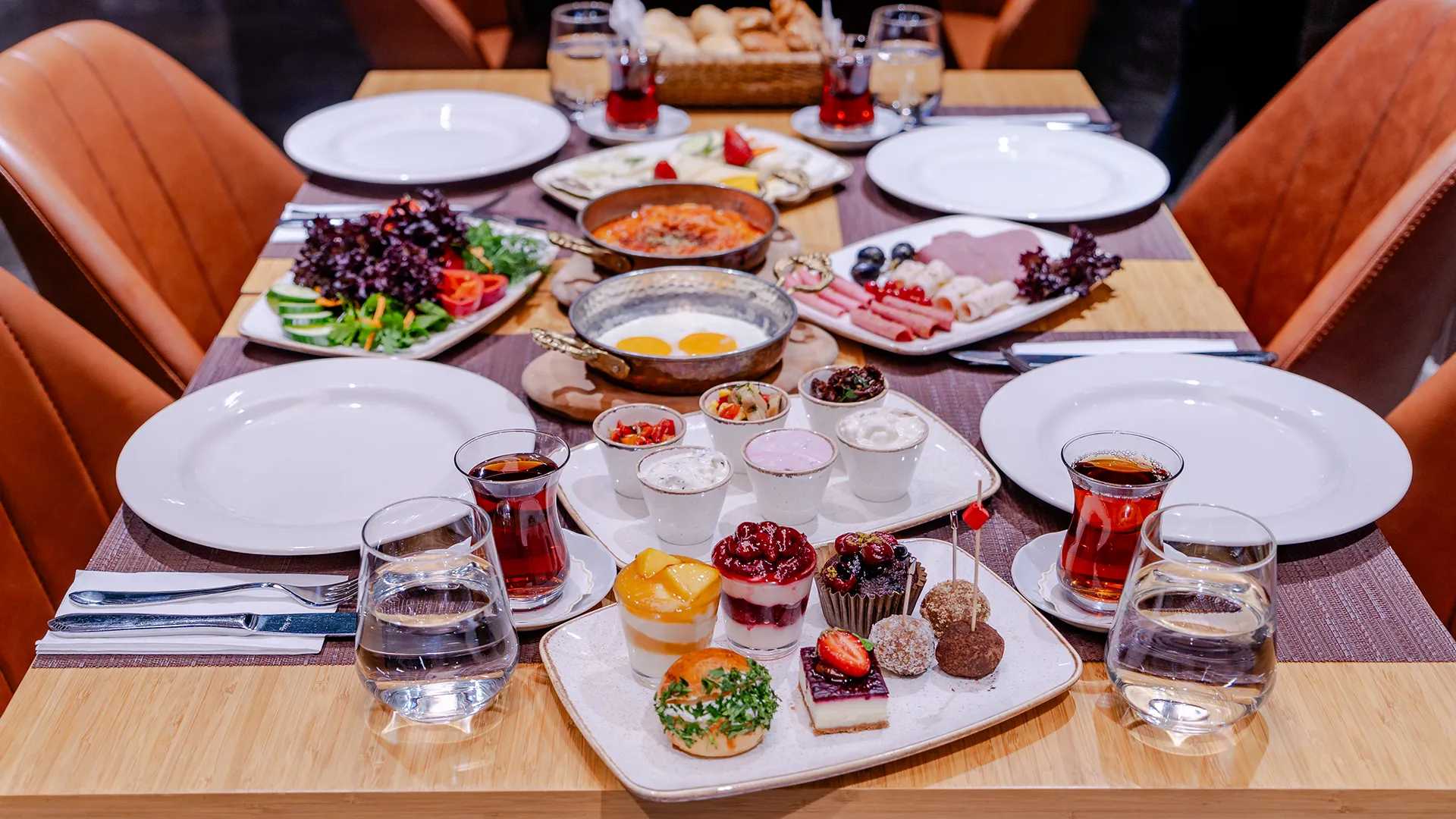 Türk kahvaltısının çeşitli lezzetleriyle dolu bir masa ve buharı tüten bir fincan Türk çayı.